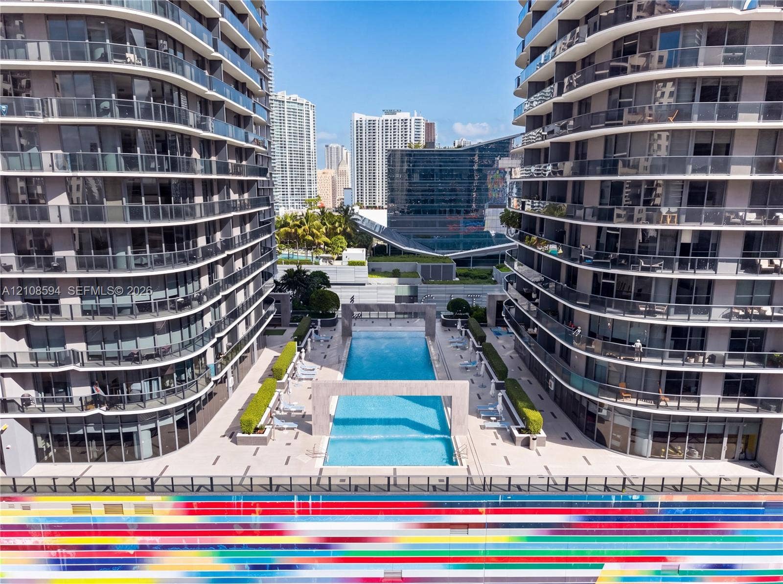 45 SW 9th Street, #2206, Miami, FL 33130 Outdoor pool featuring concrete deck surfaces, decorative stone archways, manicured hedges, and multi-story high-rise buildings with glass-paneled balconies