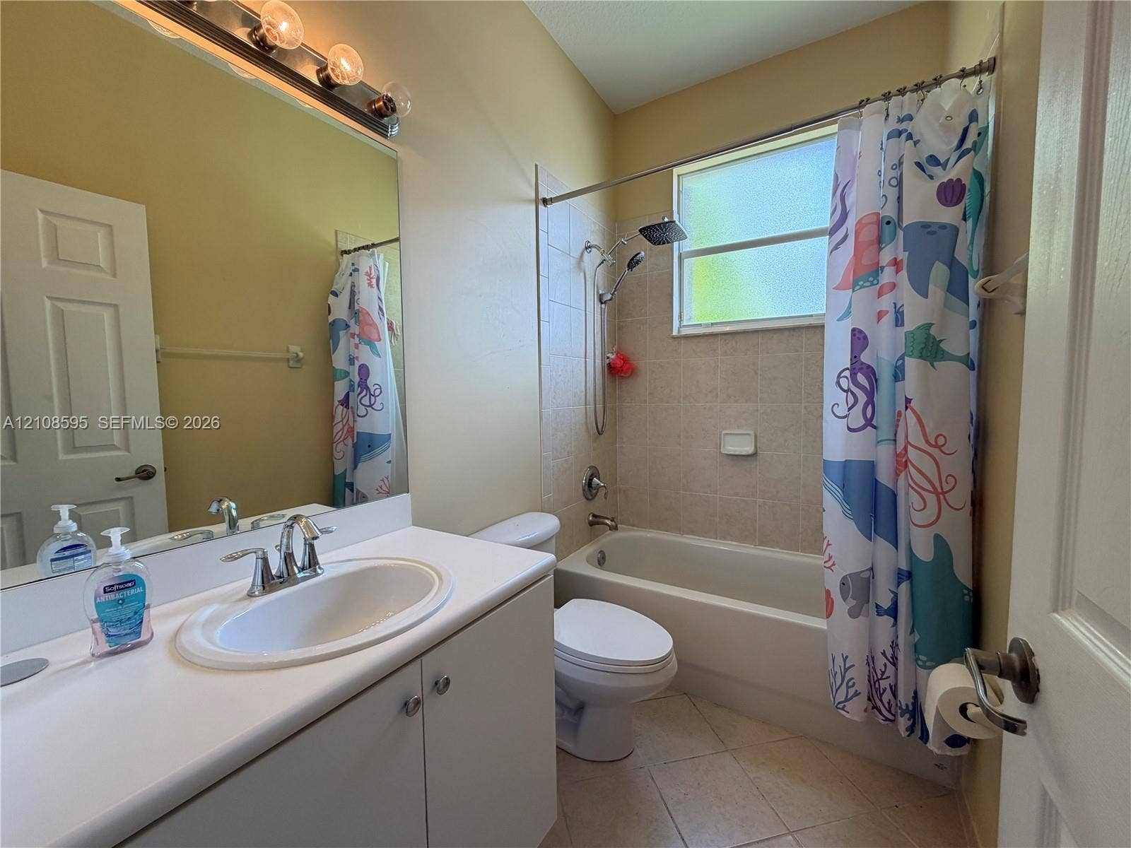 12989 SW 135th Terrace, #0, Miami, Miami, FL 33186 Full-width vanity with solid-surface countertop and integrated oval sink, porcelain bathtub with tile surround, polished chrome fixtures, and large wall-mounted mirror