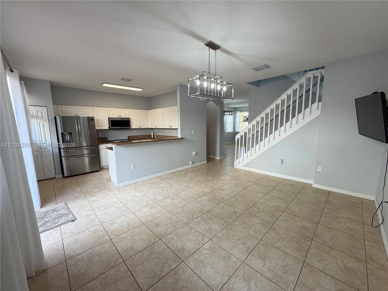 12989 SW 135th Terrace, #0, Miami, Miami, FL 33186 Open-concept space featuring ceramic tile flooring, kitchen with white cabinetry and stone countertops, stainless steel appliances, and a built-in staircase with white railings