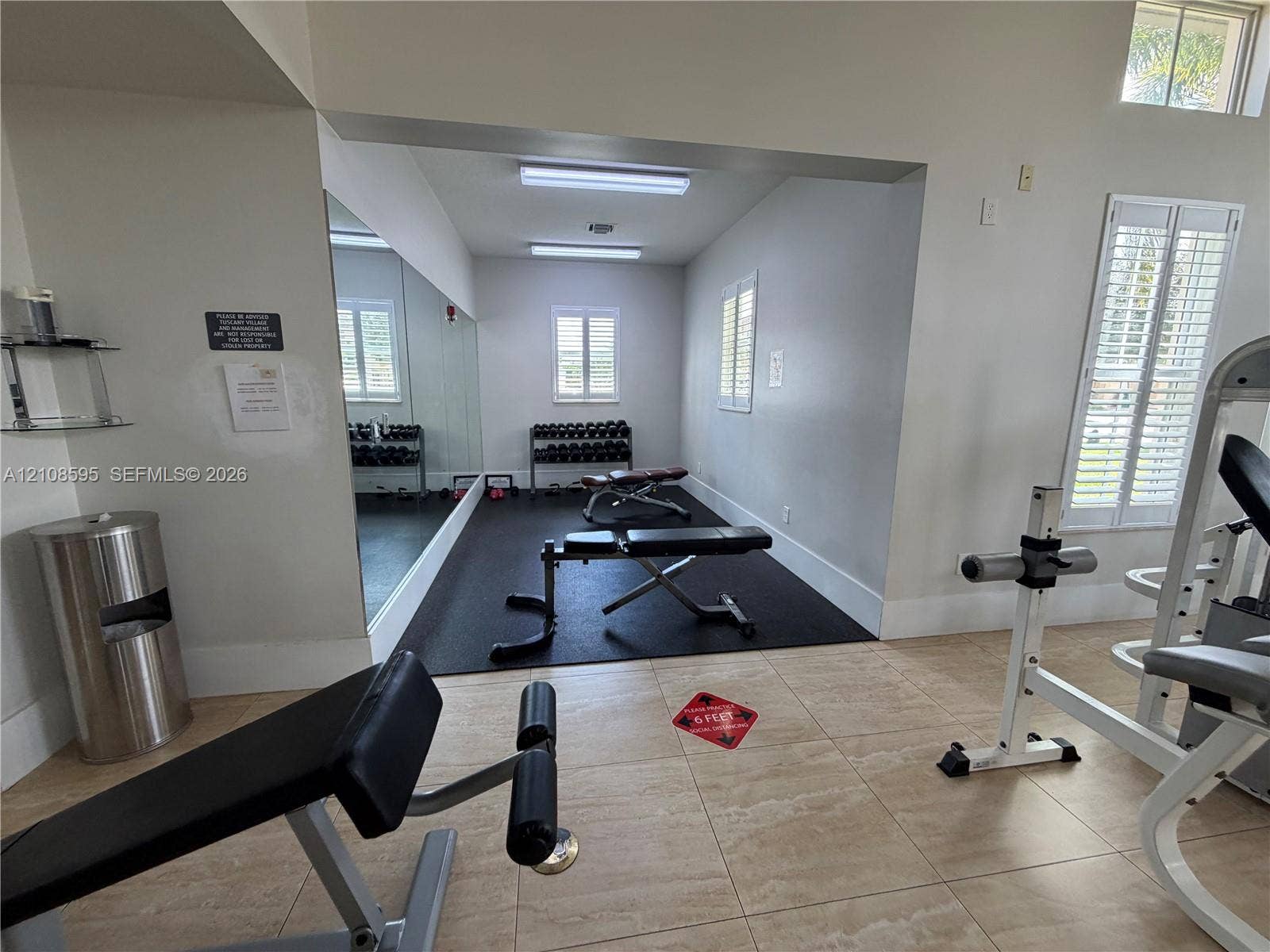12989 SW 135th Terrace, #0, Miami, Miami, FL 33186 Fitness area featuring tile flooring, a rubber-floored section, full-length wall mirror, windows with plantation shutters, and overhead fluorescent lighting