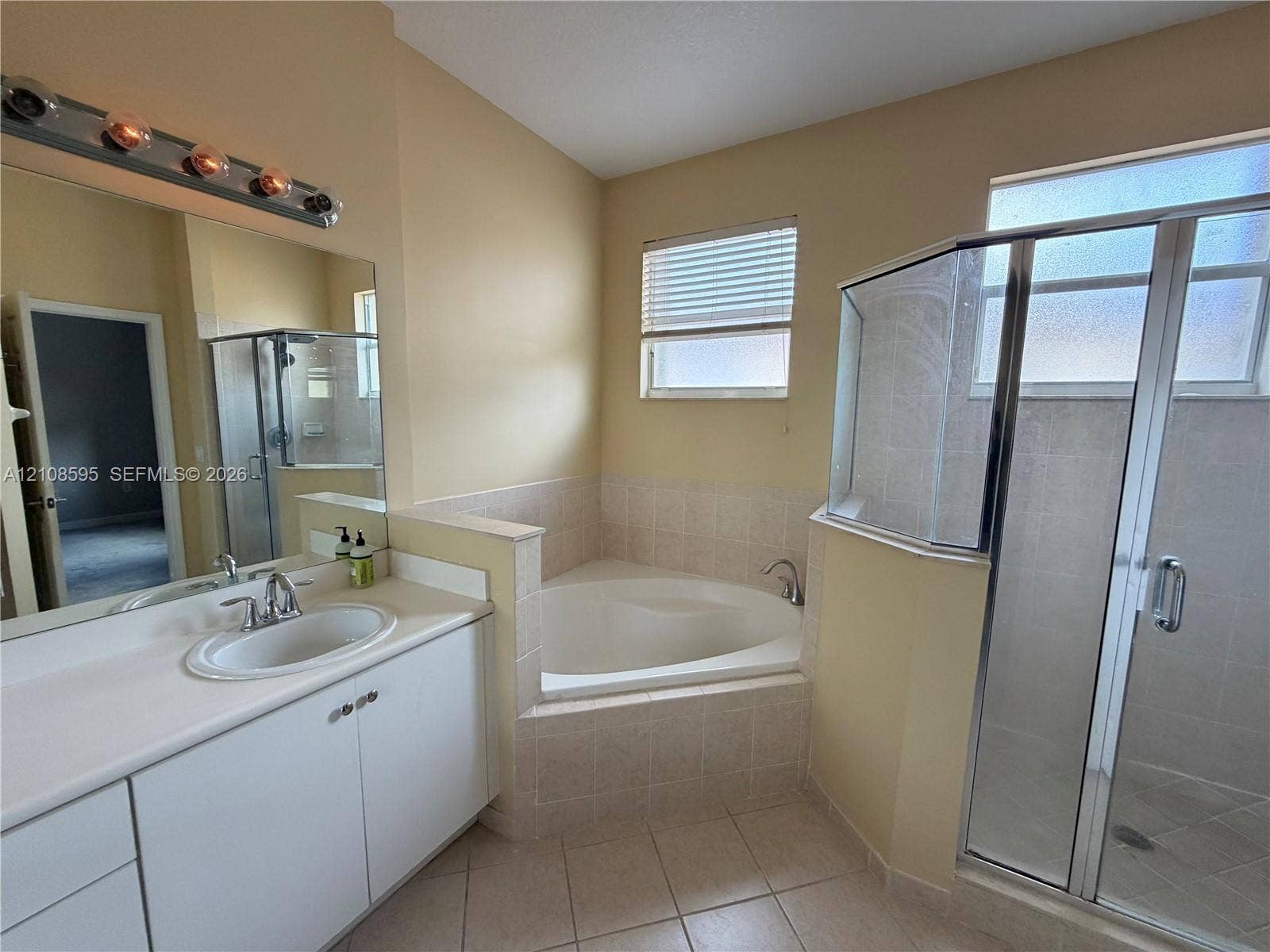 12989 SW 135th Terrace, #0, Miami, Miami, FL 33186 Bathroom featuring a white vanity with a solid-surface countertop, an oval-shaped soaking tub with tile surround, and a glass-enclosed shower with tiled flooring