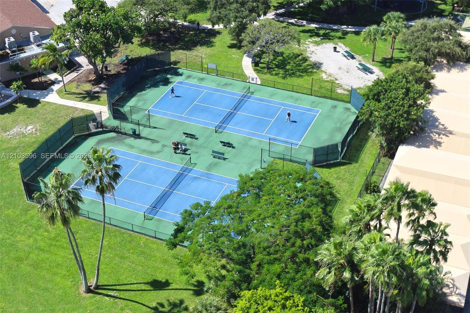 Dual tennis courts featuring hard-surface playing areas, perimeter chain-link fencing, and professional-grade netting