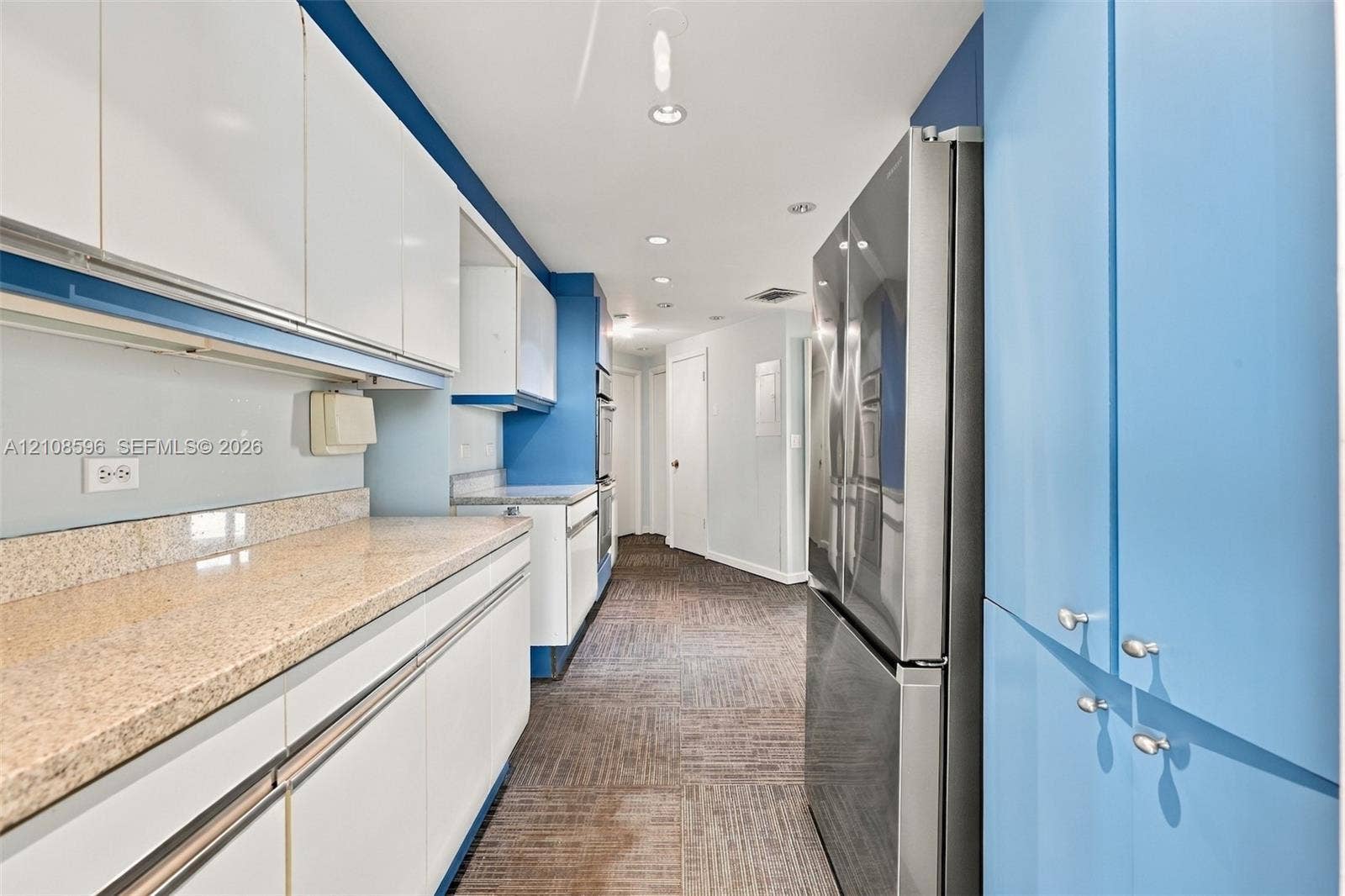 Kitchen featuring flat-panel white and blue cabinetry, speckled stone countertops, a full-height pantry, and a stainless steel refrigerator