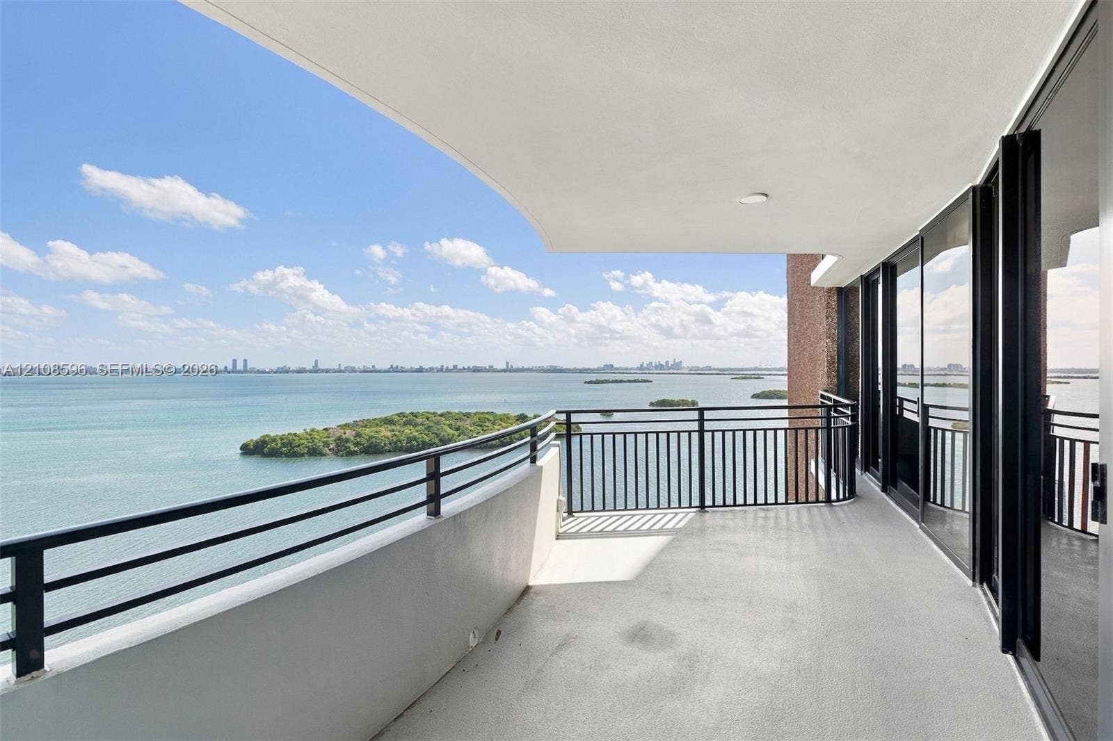 Covered balcony featuring a metal railing, concrete flooring, and sliding glass panel doors
