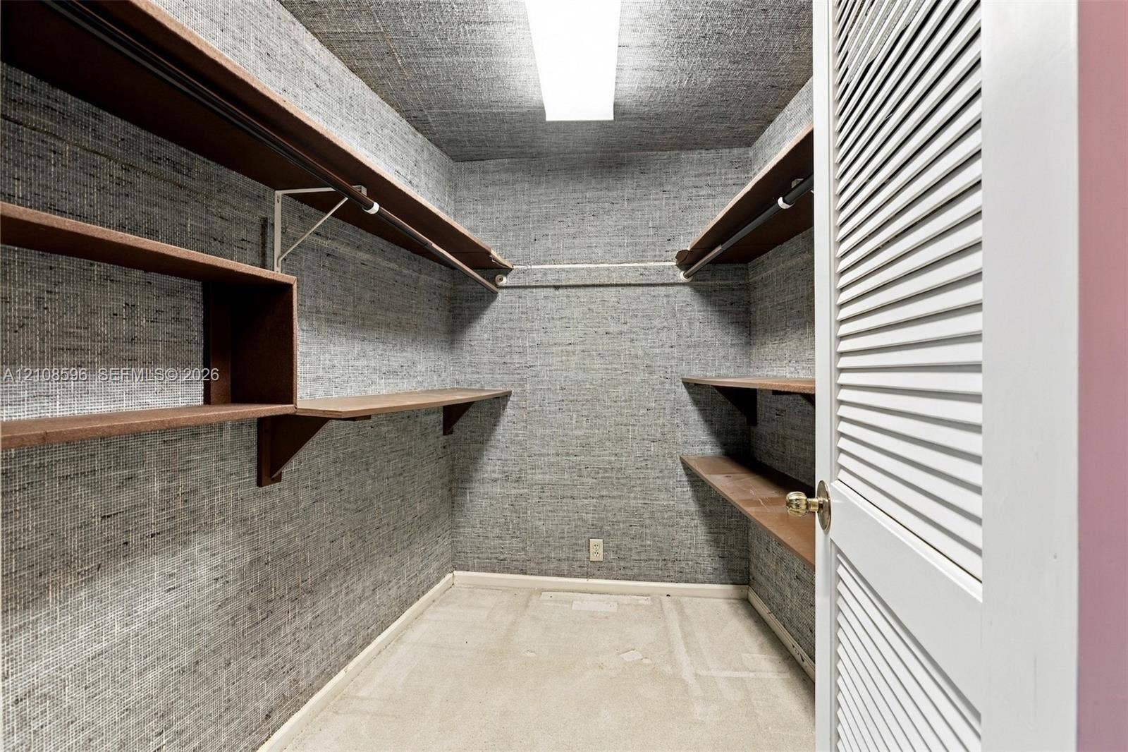 Walk-in closet featuring textured wall covering, multi-level wood-finish shelving, integrated hanging rods, and a white louvered door