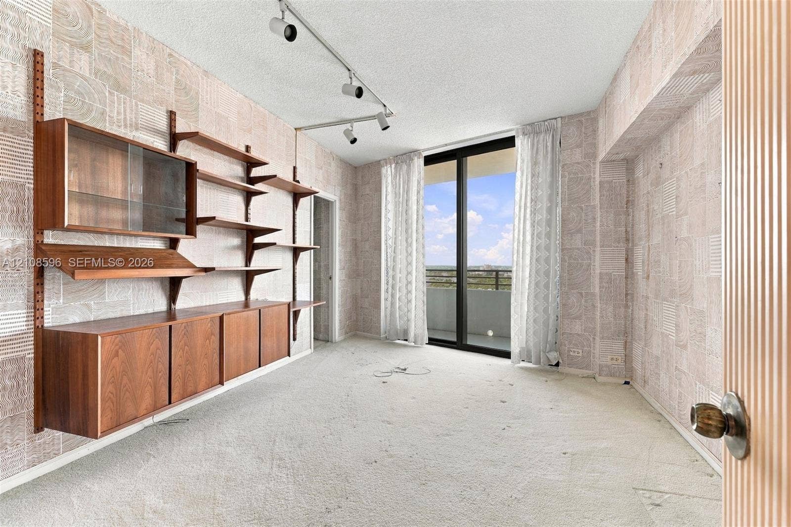 Wall-mounted wood cabinetry with shelving, track lighting, sliding glass door, and exterior balcony