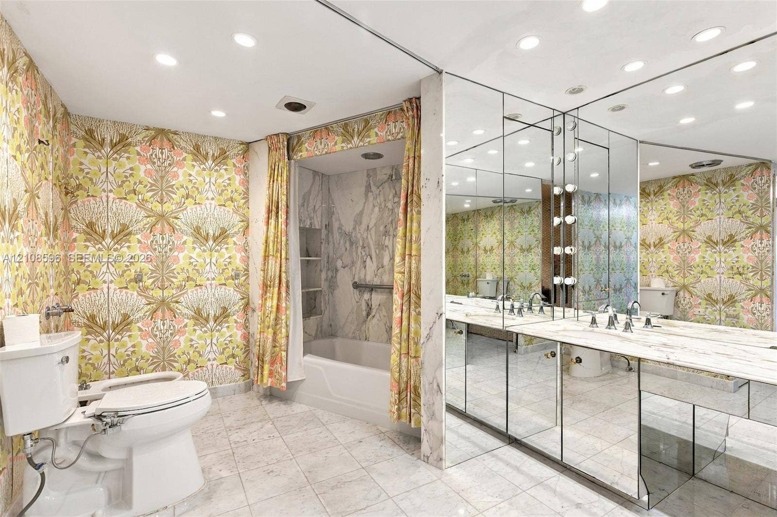 Bathroom featuring stone tile flooring, a tub-shower combination with full-height stone surround, an expansive mirrored wall, a stone vanity countertop, and recessed ceiling lighting