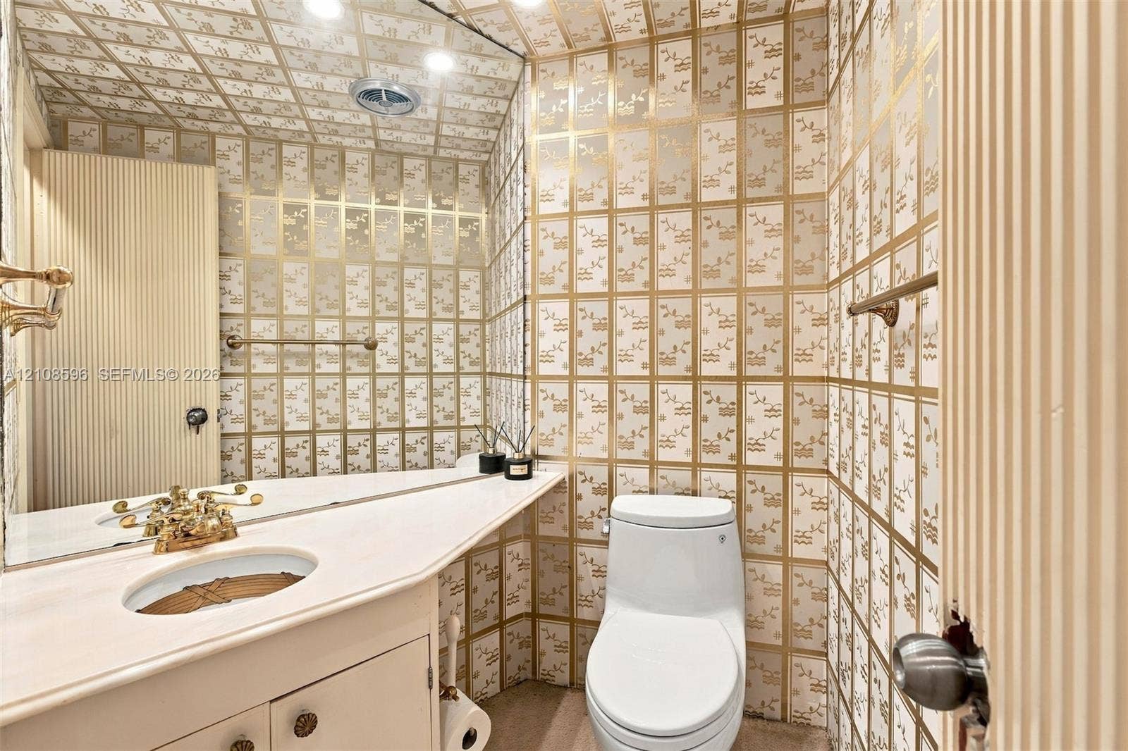 Custom vanity featuring a solid-surface countertop with an integrated oval basin and metallic-finish hardware, complemented by patterned wall-to-ceiling surfacing, a large wall-mounted mirror, and a one-piece toilet
