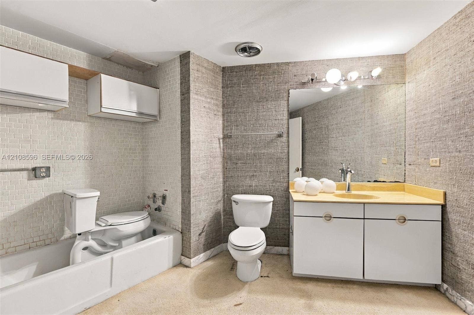 Bathroom featuring textured wall coverings, wall-mounted white cabinetry, a single vanity with integrated sink, and a combination tub and shower