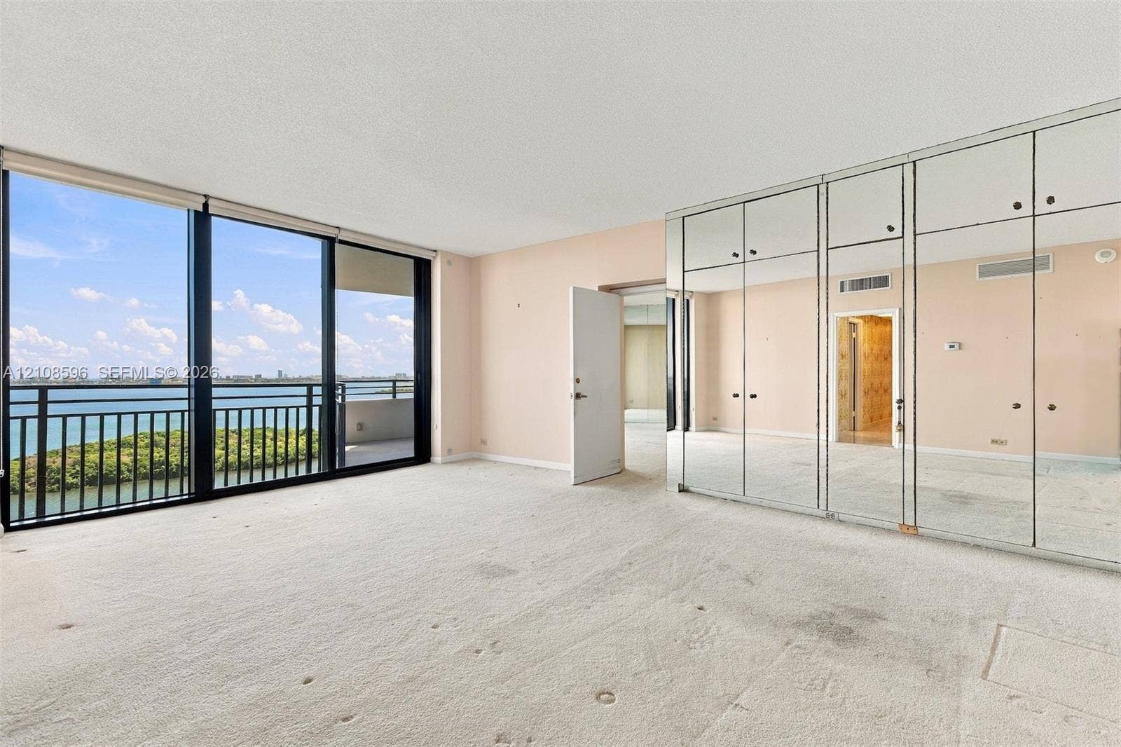 Floor-to-ceiling windows, waterfront balcony with metal railing, built-in mirrored wall cabinetry, and neutral carpeting