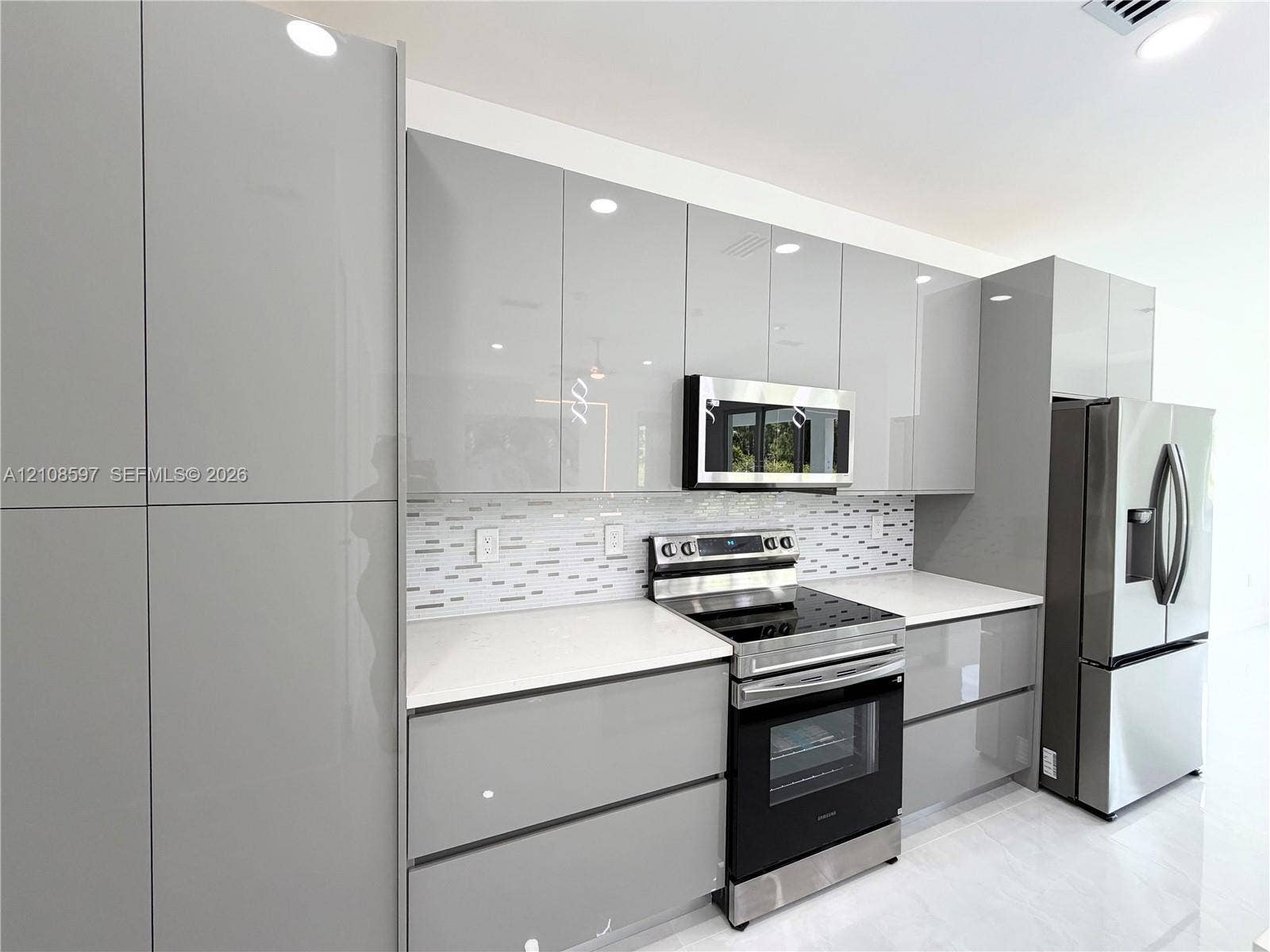 808 Congress Avenue, Lehigh Acres, FL 33972 Modern kitchen featuring high-gloss gray cabinetry, white solid-surface countertops, a mosaic tile backsplash, and stainless steel appliances