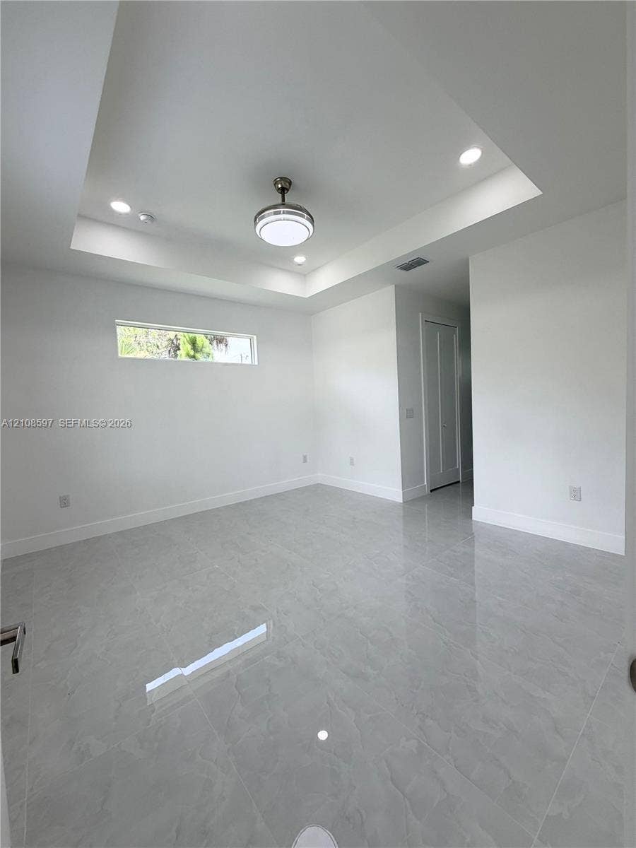 Tray ceiling with recessed lighting, large-format tile flooring, central ceiling fan, and horizontal clerestory window