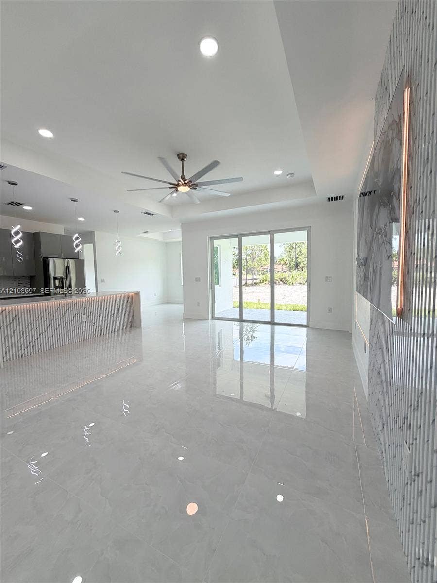 Open-concept area featuring polished stone-finish flooring, recessed lighting, a coffered ceiling with a modern multi-blade ceiling fan, and a kitchen island with stone-finish cladding