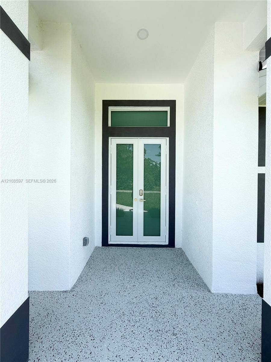 Covered entryway featuring a stippled-texture ceiling, recessed lighting, aggregate flooring, and a double-door entry with a rectangular transom window