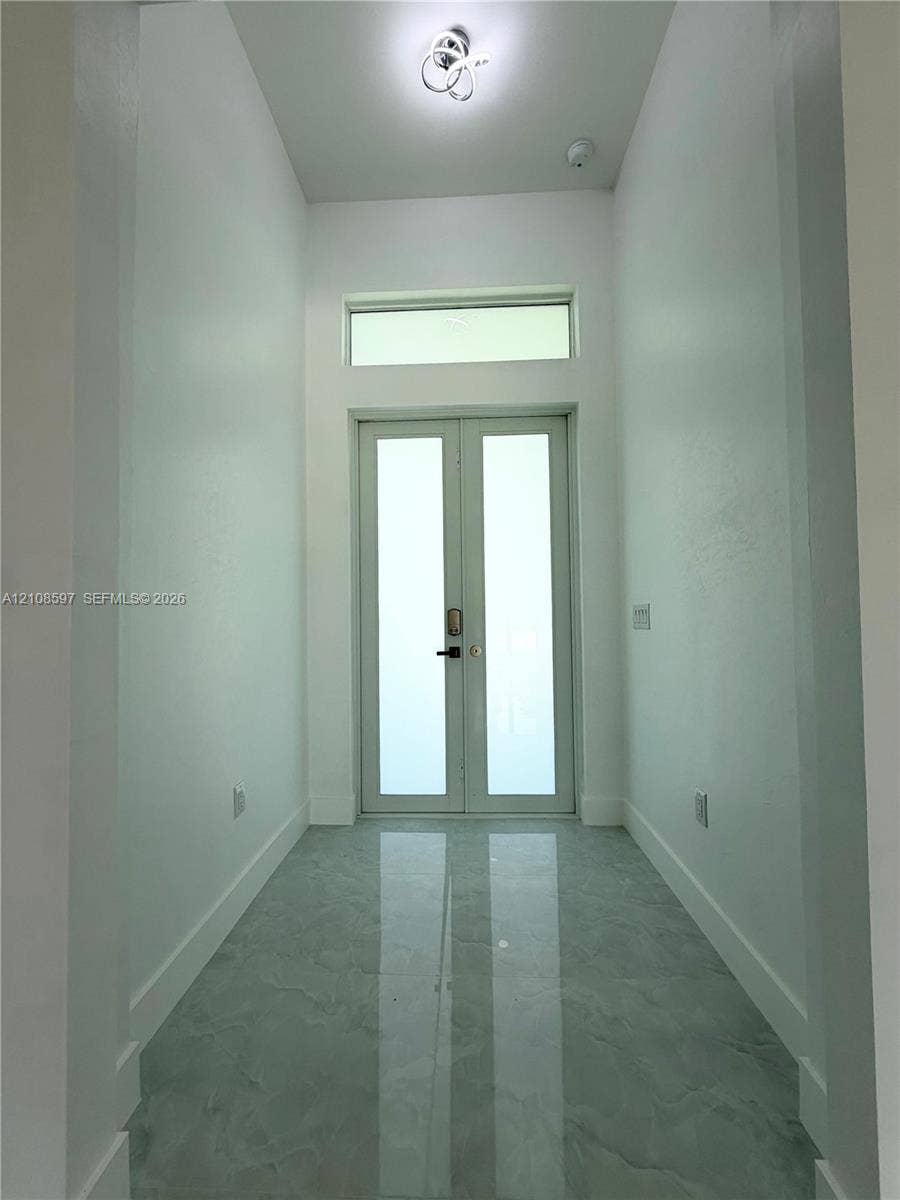 Entryway featuring double glass-paneled doors, transom window, high ceilings, large-format polished stone-finish tile flooring, and contemporary flush-mount overhead lighting