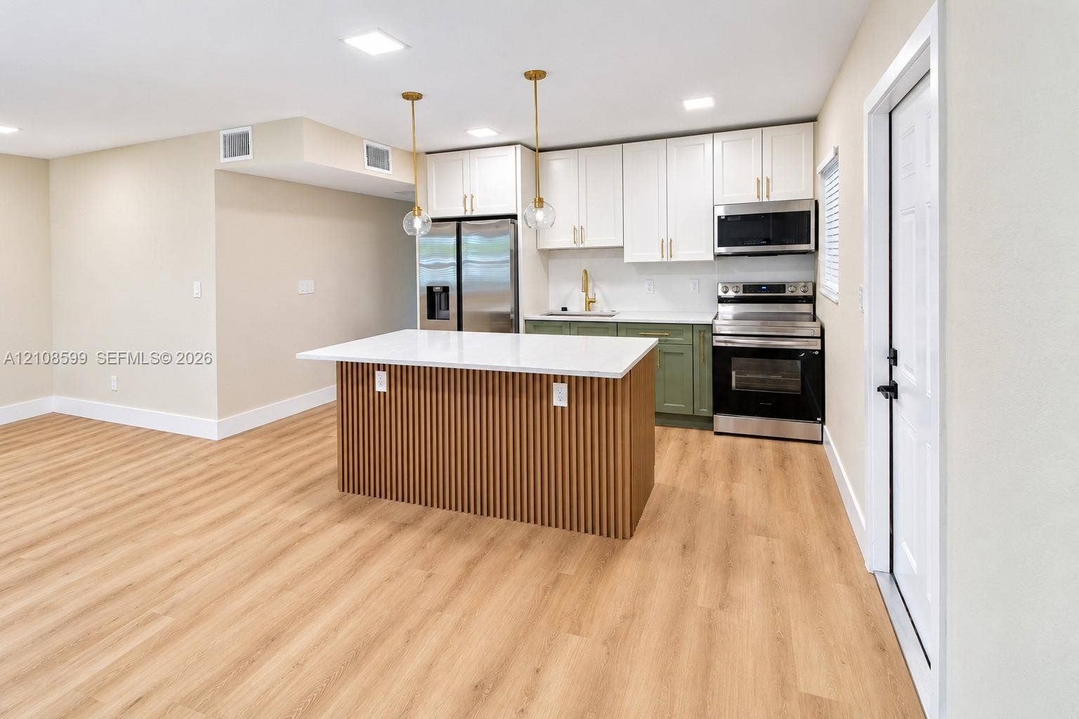 Kitchen featuring a center island with slatted wood detailing and a solid-surface countertop, two-toned shaker-style cabinetry, stainless steel appliances, and wood-finish flooring