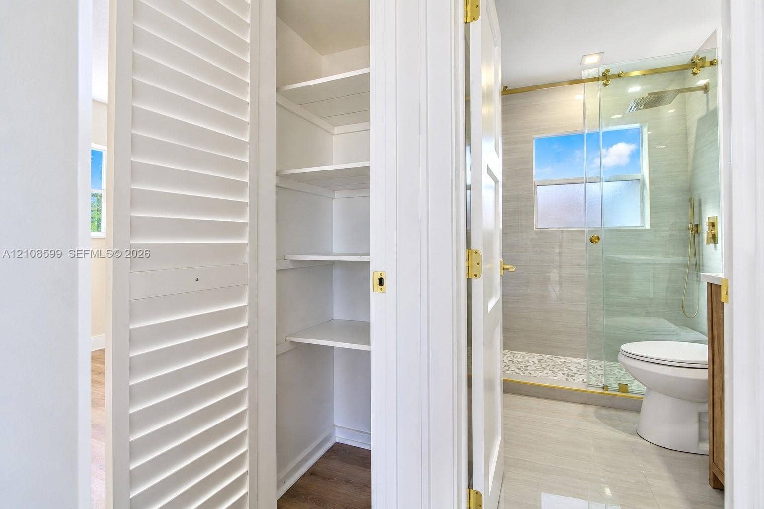 Built-in white storage cabinetry, walk-in shower with glass enclosure, metallic gold-finish hardware, and tile flooring