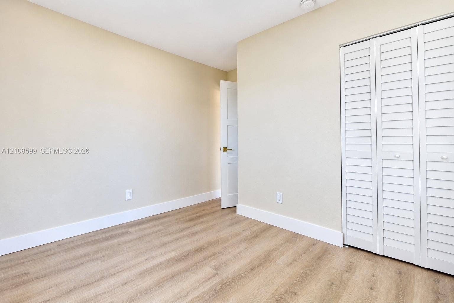 Interior room featuring wood-finish flooring, white louvered closet doors, and neutral wall paint