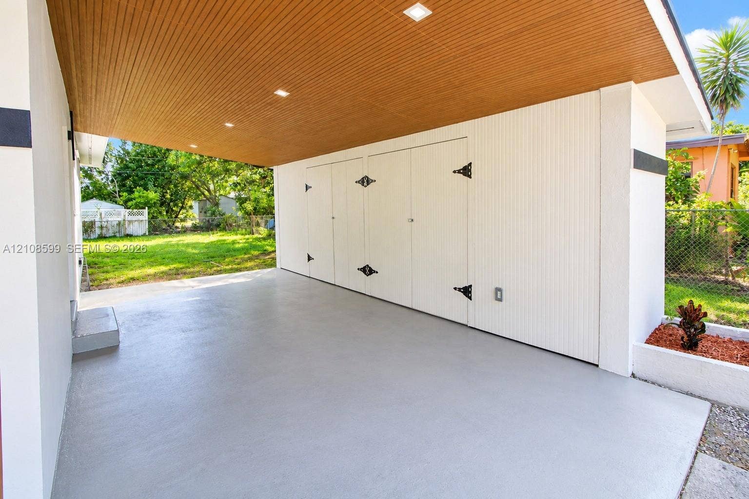 Covered carport featuring a wood-slat ceiling, recessed lighting, concrete flooring, and integrated storage cabinetry with decorative hardware