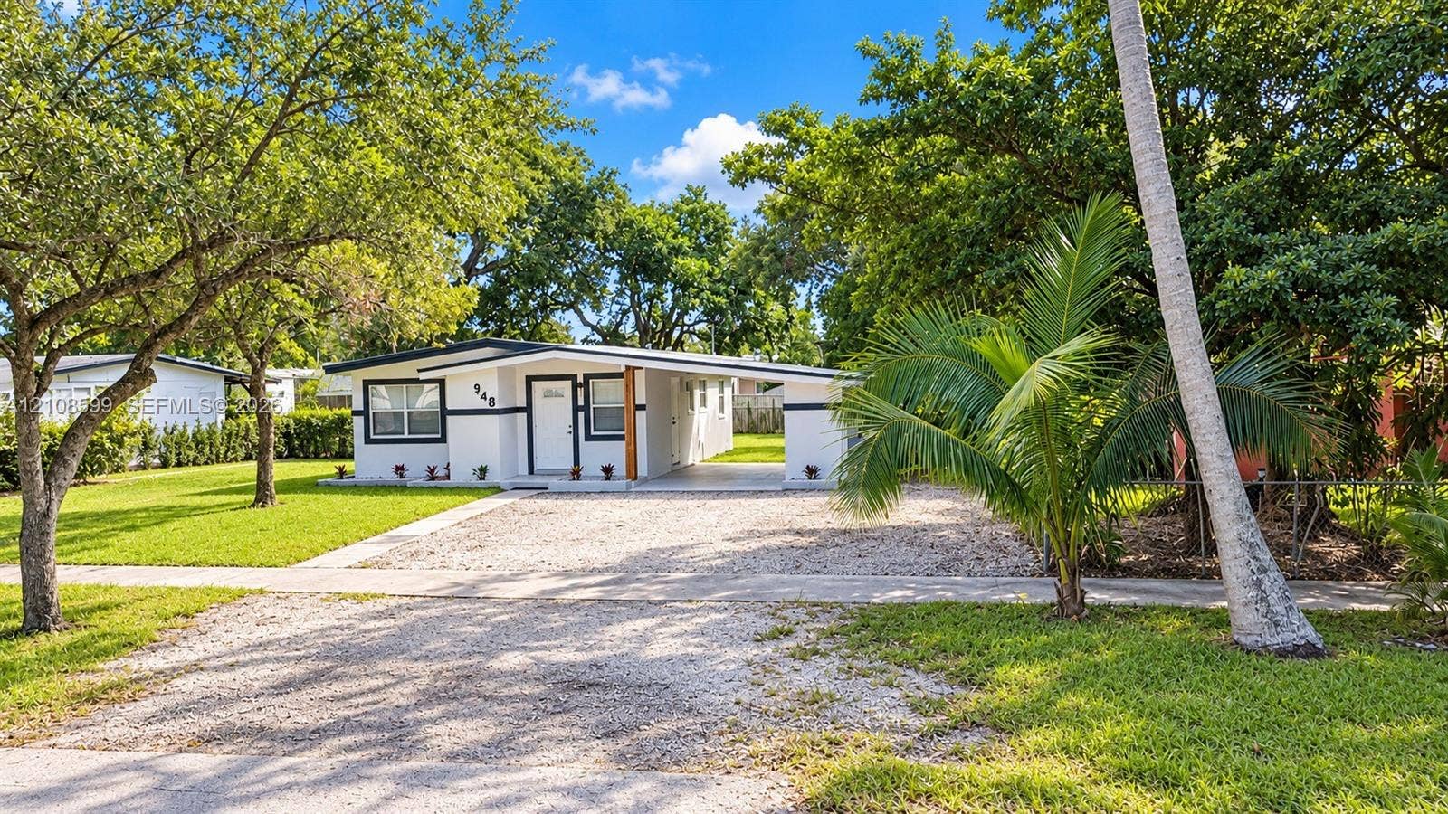 Single-story exterior featuring white stucco siding with dark trim, a stone-surfaced driveway, and a covered carport