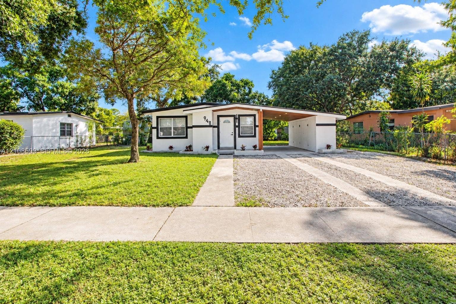 Single-story exterior featuring a stucco facade, attached carport, gravel driveway, and manicured lawn