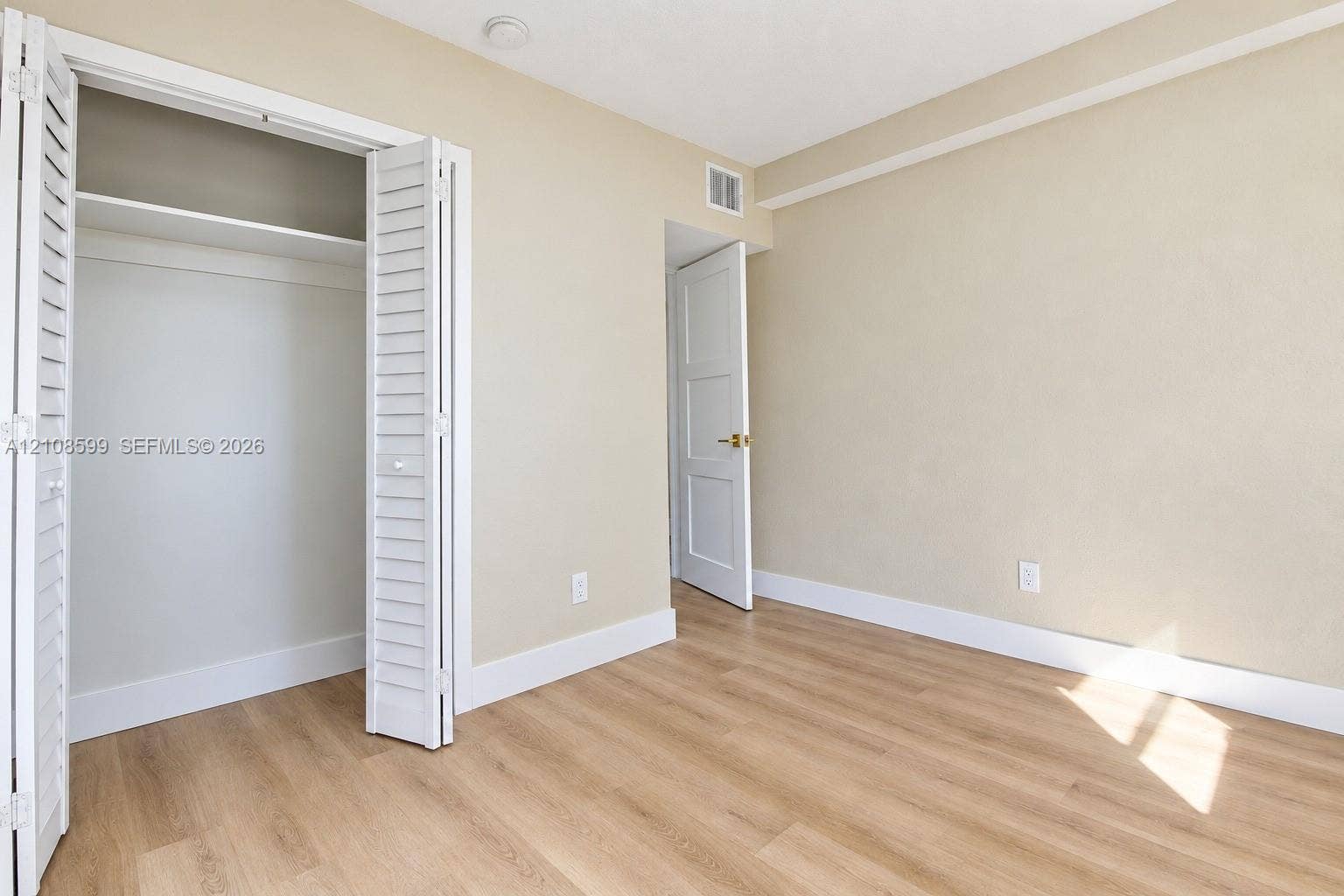 Interior space featuring wood-finish flooring, a closet with louvered bi-fold doors, and a paneled interior door with gold-tone hardware