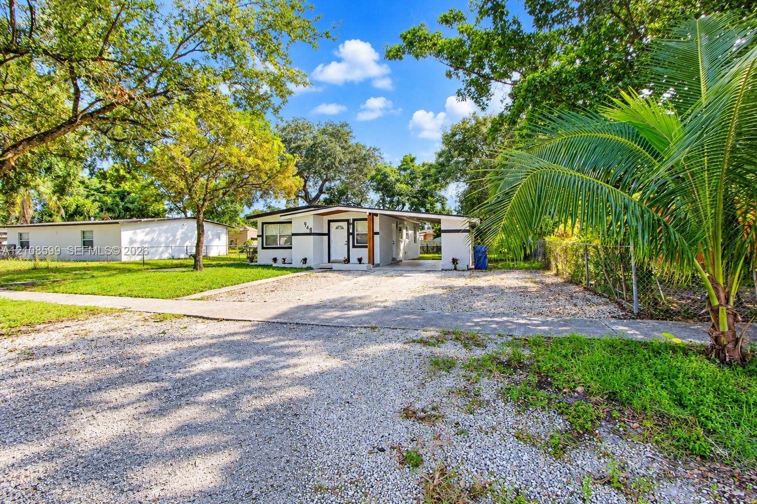 Single-story exterior featuring a stone-aggregate driveway, attached carport, mature landscaping, and light-colored siding