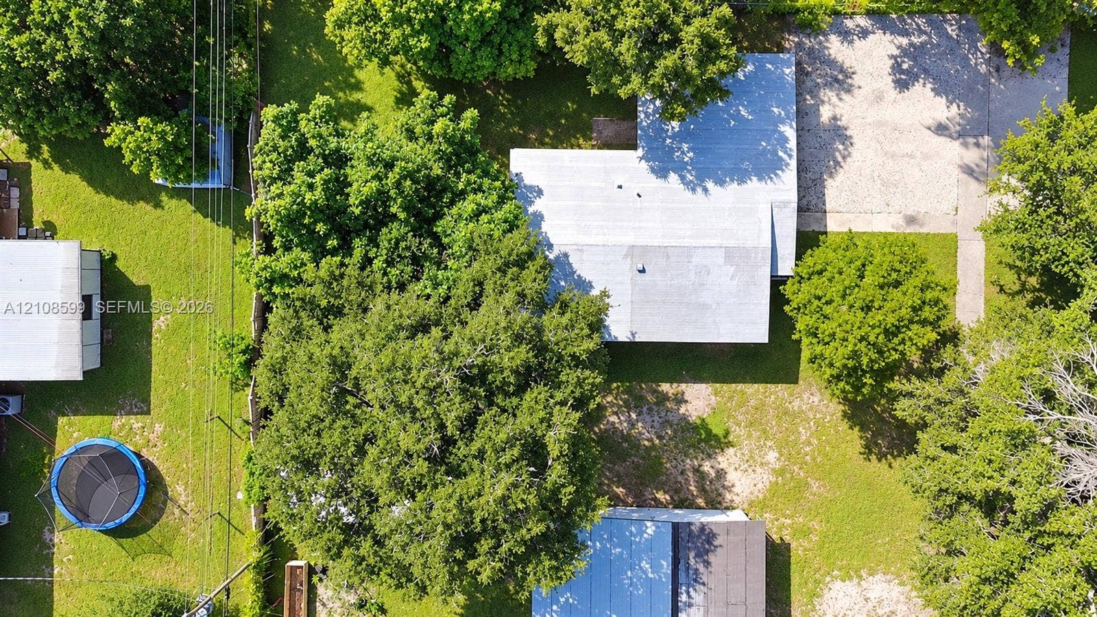 Aerial perspective of a property featuring expansive green space, mature canopy trees, a dedicated gravel driveway, and detached structural elements on a level lot
