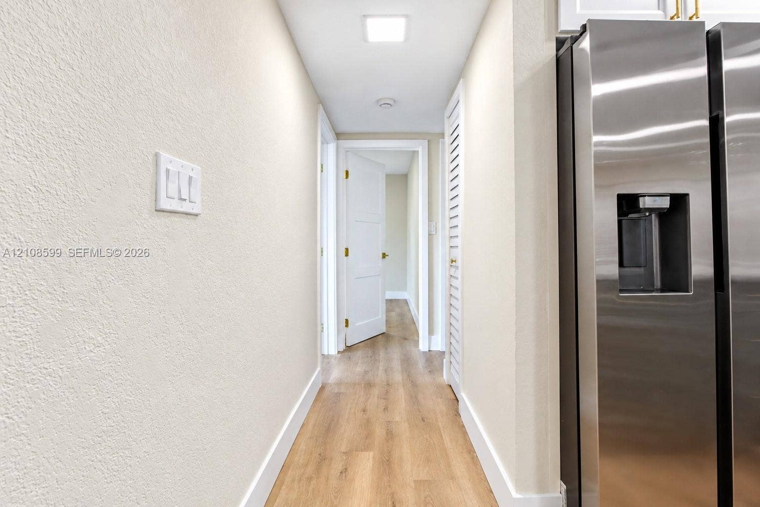 Stainless steel refrigerator, wood-finish flooring, white panel doors, and louvered closet doors