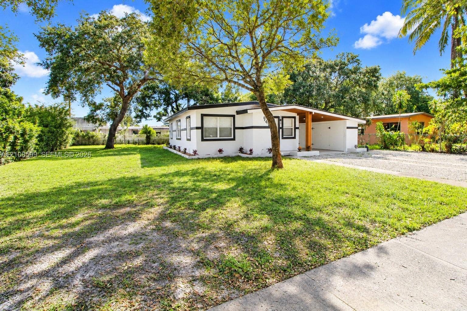 Single-story exterior featuring white stucco siding with dark trim, a covered front entryway, exposed wood support beam, and an expansive lawn