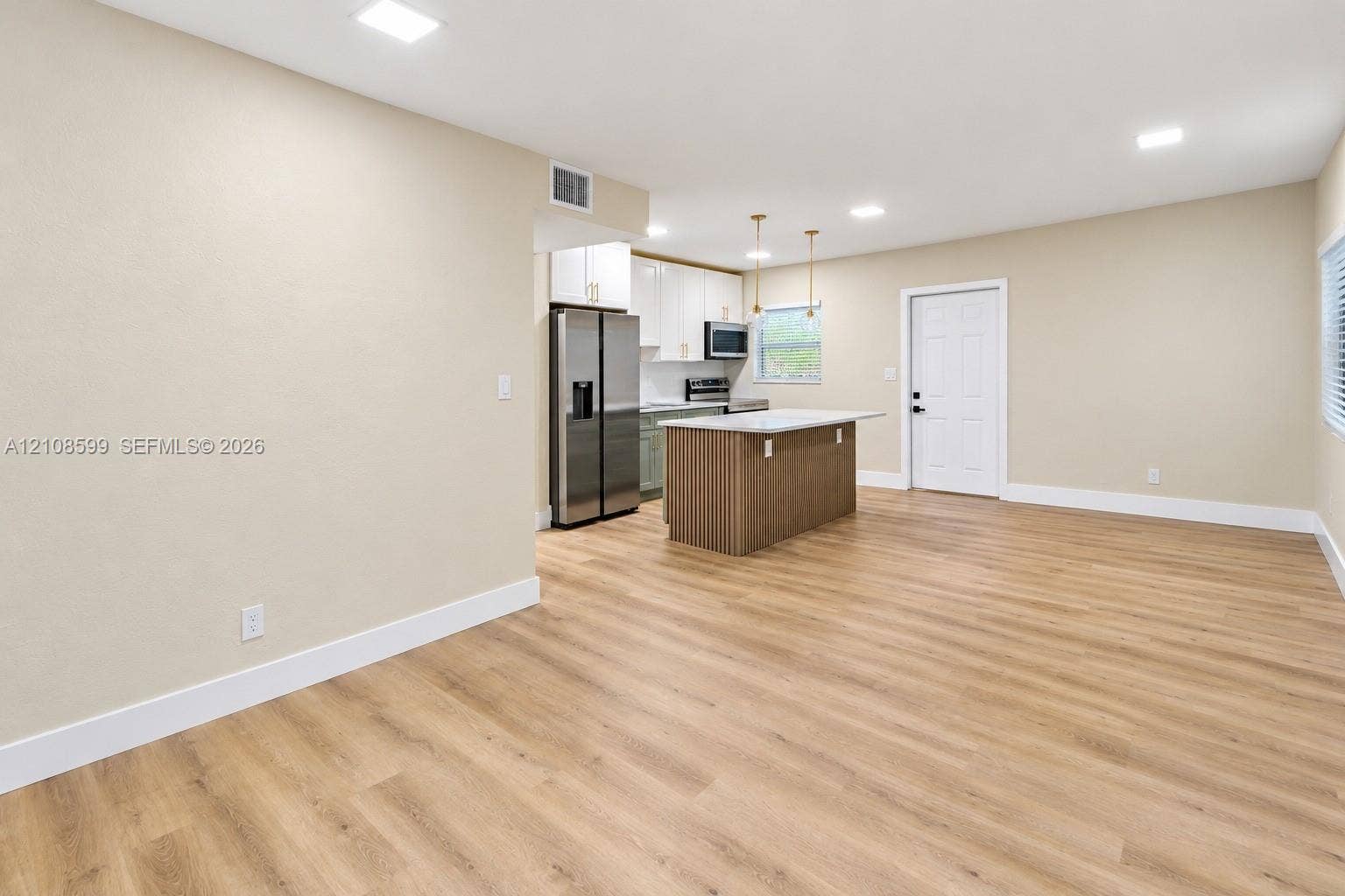 Open-concept kitchen featuring wood-finish flooring, a central island with a countertop, stainless steel refrigerator, white cabinetry, and recessed lighting