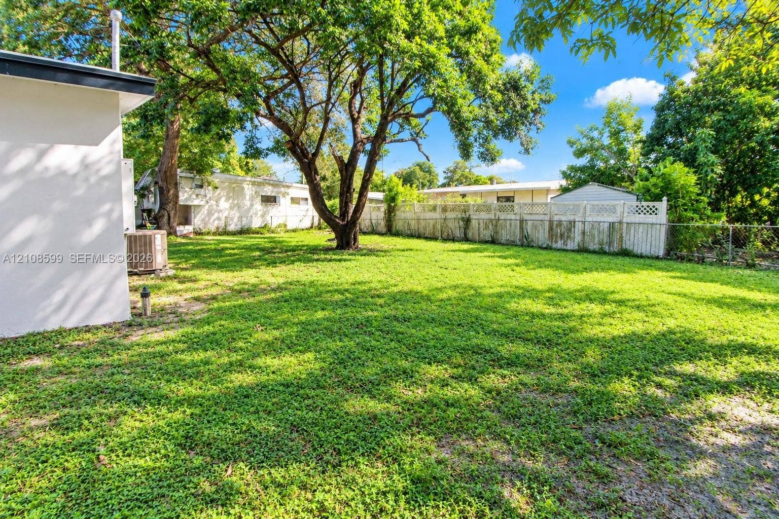 Expansive backyard featuring a lush lawn, mature trees, and a white privacy fence