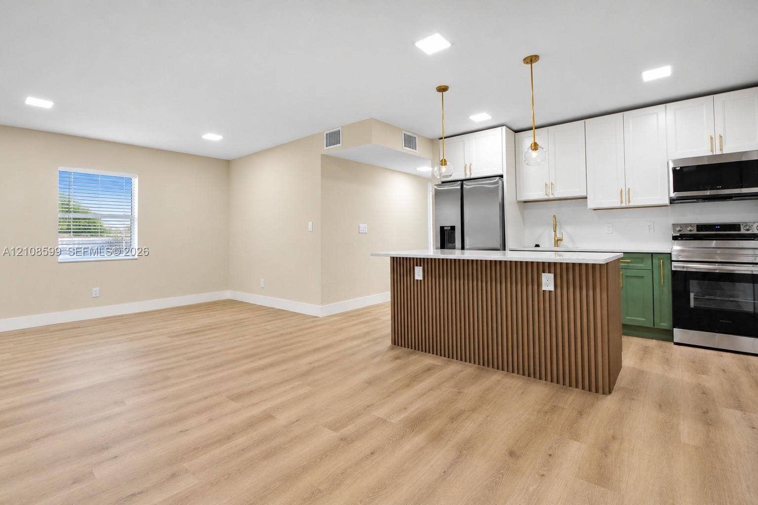Kitchen featuring a slatted wood-finish island, white and green cabinetry, stainless steel appliances, and wood-finish flooring