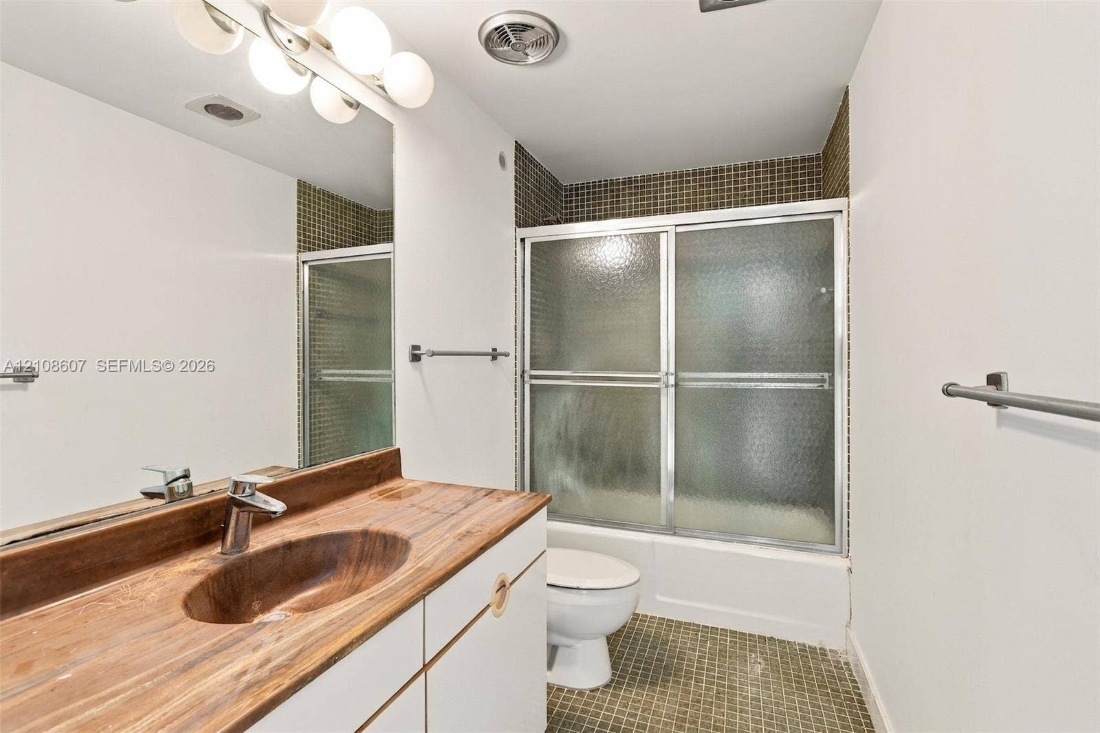 Bathroom featuring a wood-finish vanity countertop with an integrated oval sink, a wall-to-wall vanity mirror, a tub-shower combination with sliding glass doors, and tiled flooring