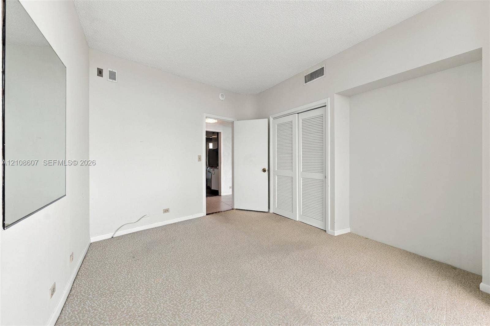 Room featuring neutral wall-to-wall carpeting, a large wall-mounted mirror, and a double-door closet with louvered panels