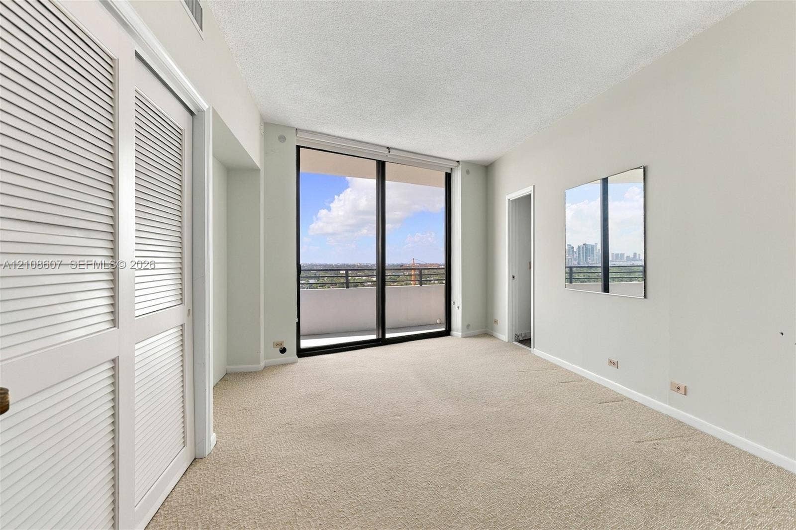 Interior space featuring floor-to-ceiling sliding glass doors, private balcony, dual-paneled louvered closet doors, and wall-mounted mirror