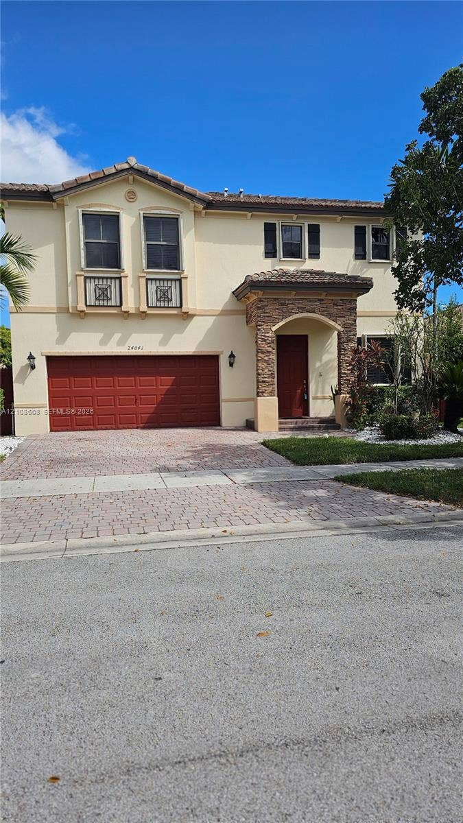 24041 SW 114th Place, Homestead, FL 33032 Two-story exterior featuring a stone-veneer entryway, paver driveway, tiled roof, decorative balcony railings, and a multi-panel garage door