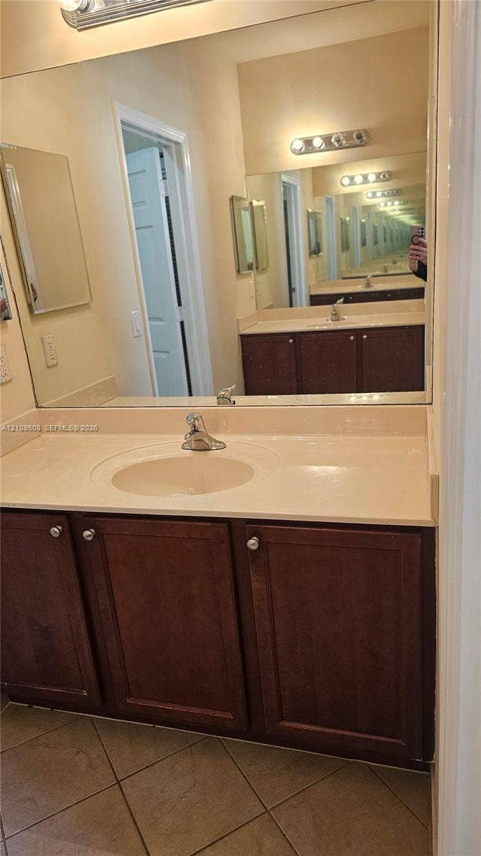 24041 SW 114th Place, Homestead, FL 33032 Bathroom vanity featuring wood-finish cabinetry, a solid surface countertop with an integrated basin, a large wall-mounted mirror, and multi-bulb vanity lighting