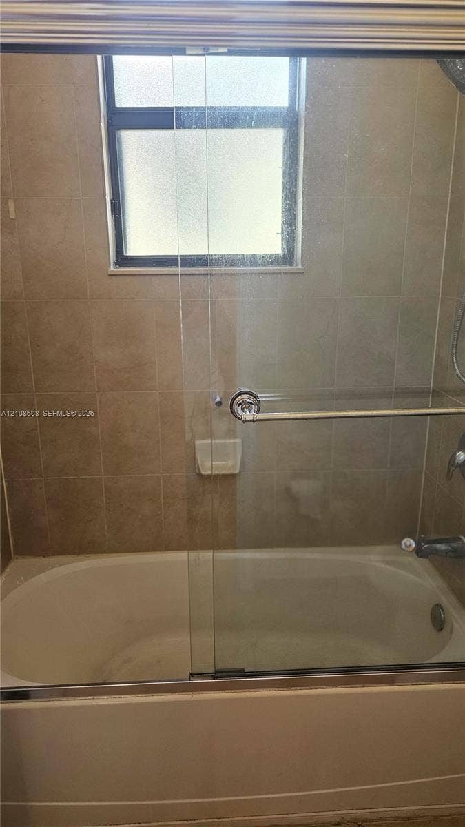 24041 SW 114th Place, Homestead, FL 33032 Bathtub and shower combination featuring neutral-toned wall tile, a sliding glass door enclosure, built-in soap niche, and a window with privacy glass