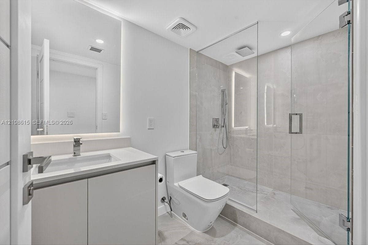 9455 Collins Avenue, #1201, Surfside, FL 33154 Modern bathroom featuring a floating vanity with a light-toned countertop, a seamless walk-in shower with a glass enclosure, large-format tile flooring, and backlit wall mirror