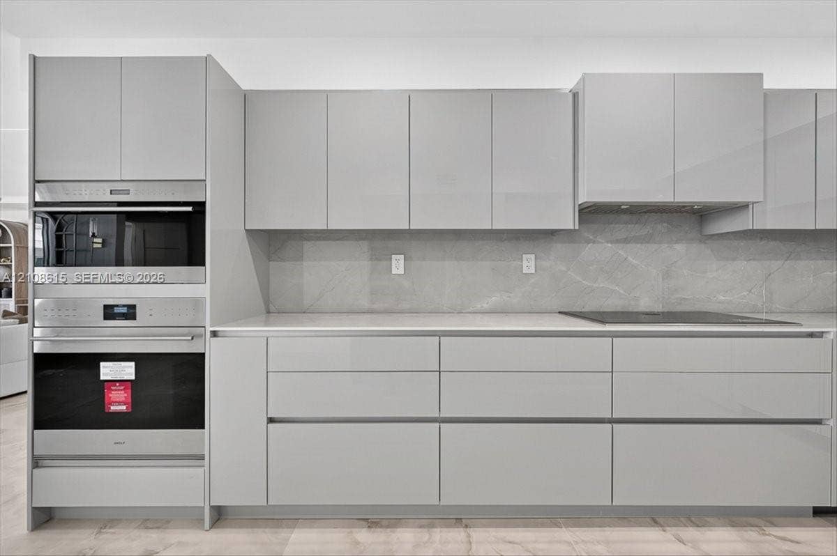 9455 Collins Avenue, #1201, Surfside, FL 33154 High-gloss cabinetry, stainless steel double wall ovens, expansive light-toned countertops, stone-finish slab backsplash, and integrated cooktop