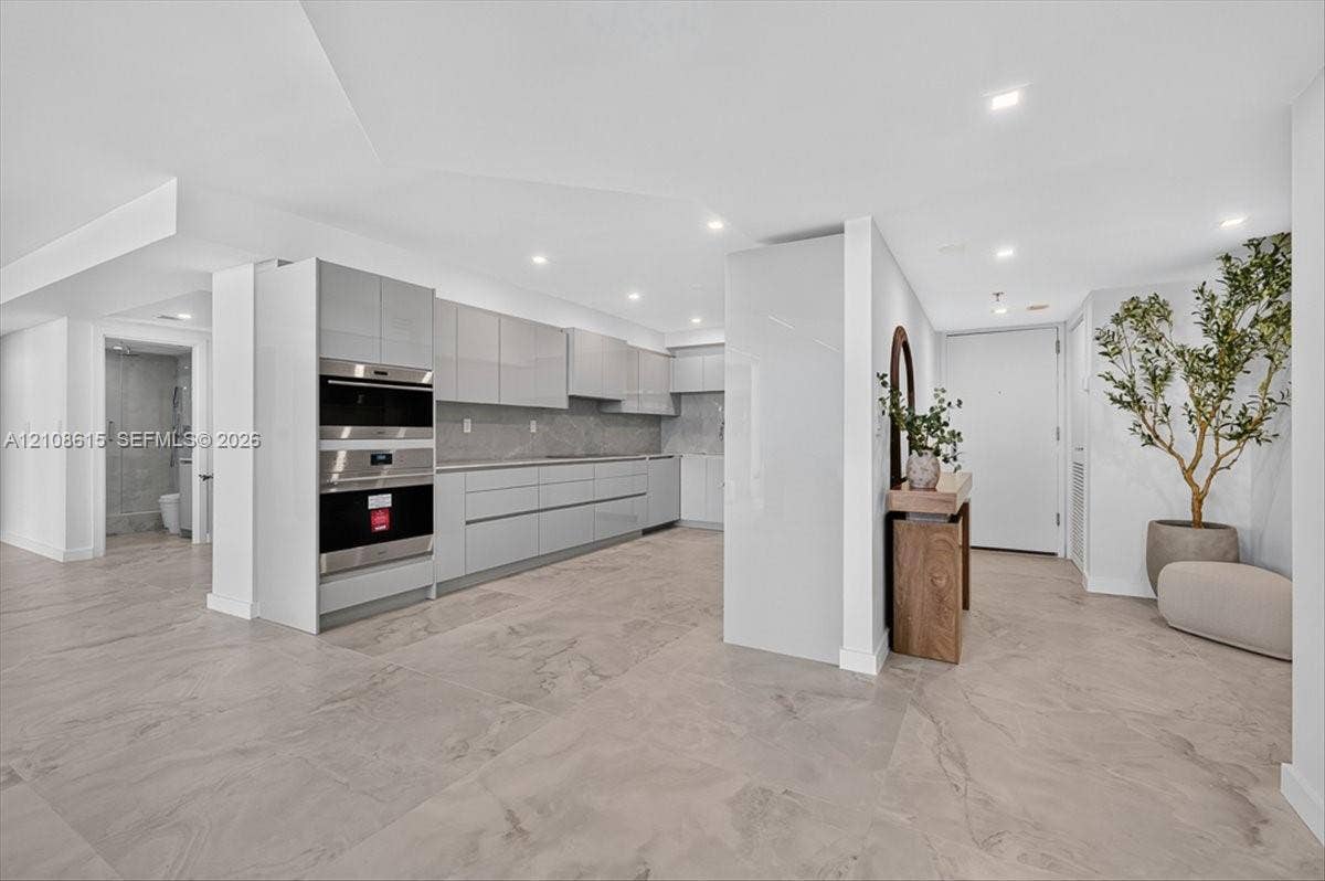 9455 Collins Avenue, #1201, Surfside, FL 33154 Modern kitchen featuring high-gloss cabinetry, stone-surface countertops, built-in double ovens, and large-format tile flooring with recessed lighting