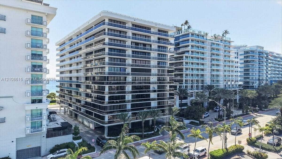 9455 Collins Avenue, #1201, Surfside, FL 33154 Multi-story residential building featuring glass-railed balconies, a concrete exterior facade, and mature palm tree landscaping