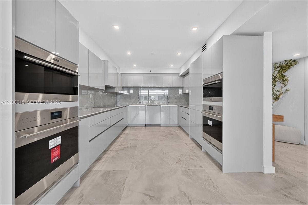 9455 Collins Avenue, #1201, Surfside, FL 33154 Contemporary kitchen featuring high-gloss cabinetry, stainless steel double wall ovens, integrated appliances, stone-finish backsplash, and large-format neutral tile flooring