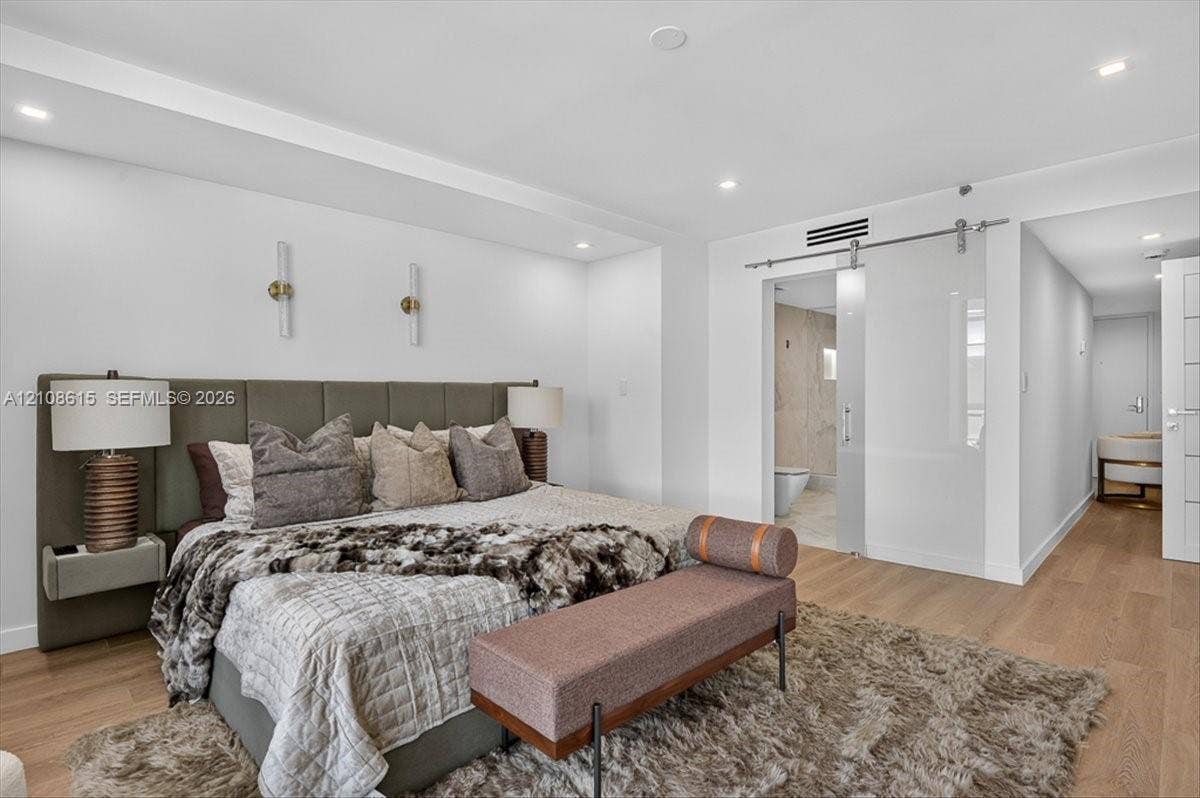9455 Collins Avenue, #1201, Surfside, FL 33154 Wood-finish flooring, recessed lighting, wall-mounted light fixtures, and a glass sliding barn door with brushed metal hardware