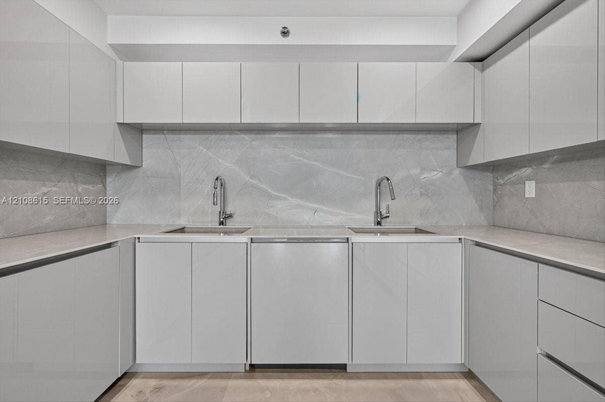 9455 Collins Avenue, #1201, Surfside, FL 33154 Glossy cabinetry, stone slab backsplash, dual undermount sinks, gooseneck faucets, and light-toned countertop surfaces
