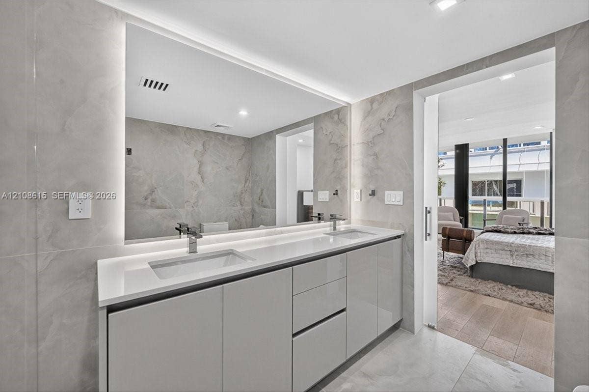 9455 Collins Avenue, #1201, Surfside, FL 33154 Floating dual-vanity with integrated sinks, quartz countertop, backlit vanity mirror, and floor-to-ceiling stone wall tiling