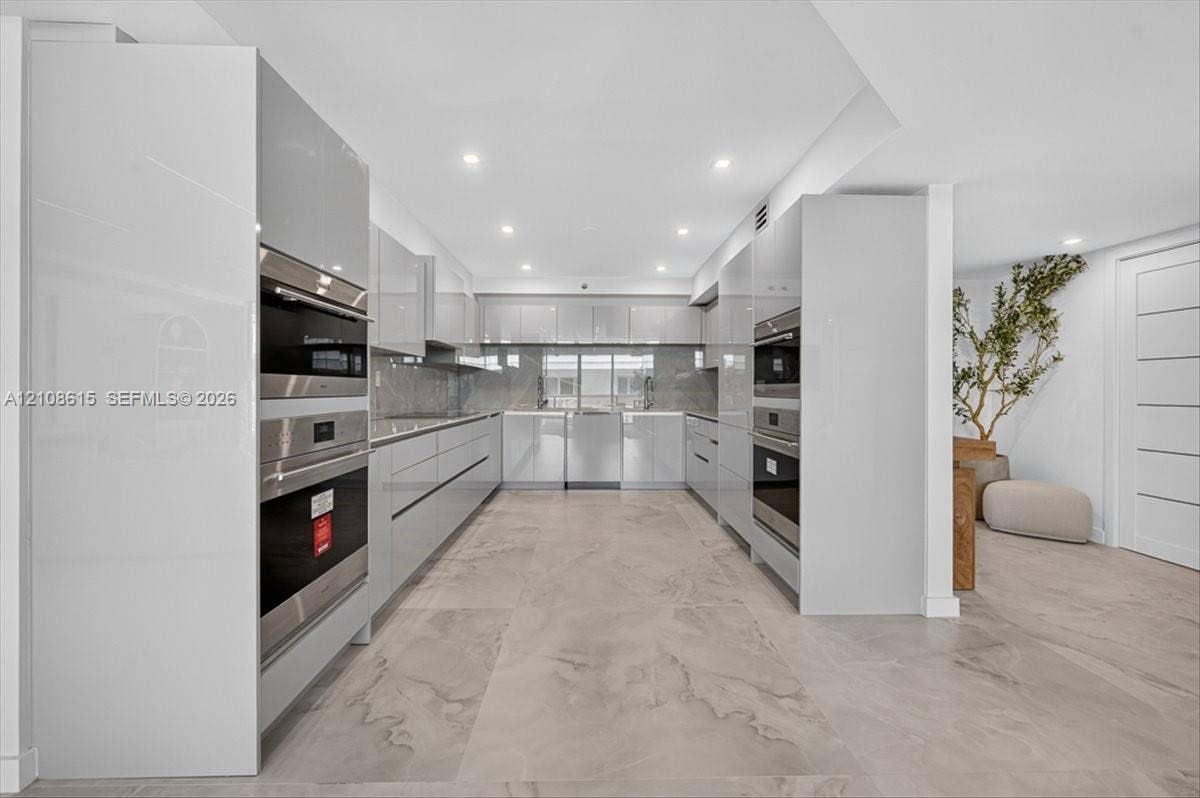 9455 Collins Avenue, #1201, Surfside, FL 33154 Contemporary kitchen featuring high-gloss cabinetry, built-in stainless steel double ovens, integrated appliances, and large-format tile flooring with recessed lighting
