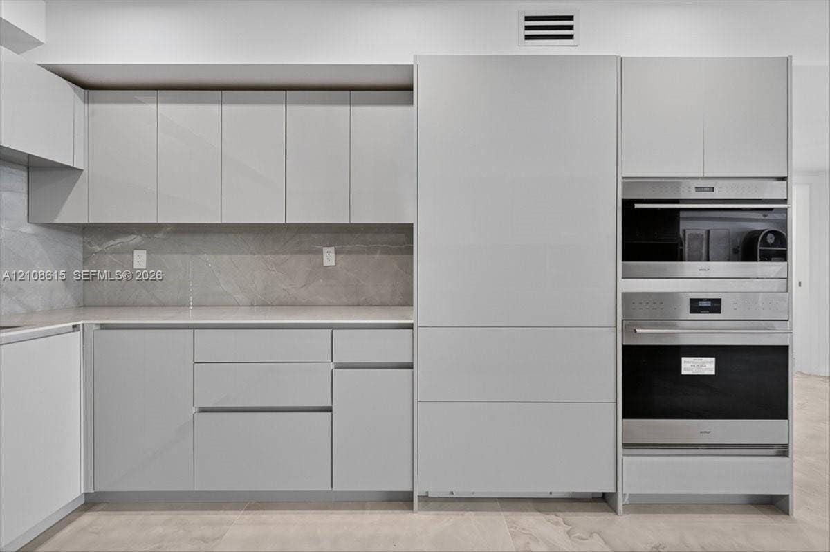 9455 Collins Avenue, #1201, Surfside, FL 33154 Modern kitchen featuring flat-panel cabinetry, stone-finish backsplash, neutral-toned countertops, and integrated stainless steel wall ovens