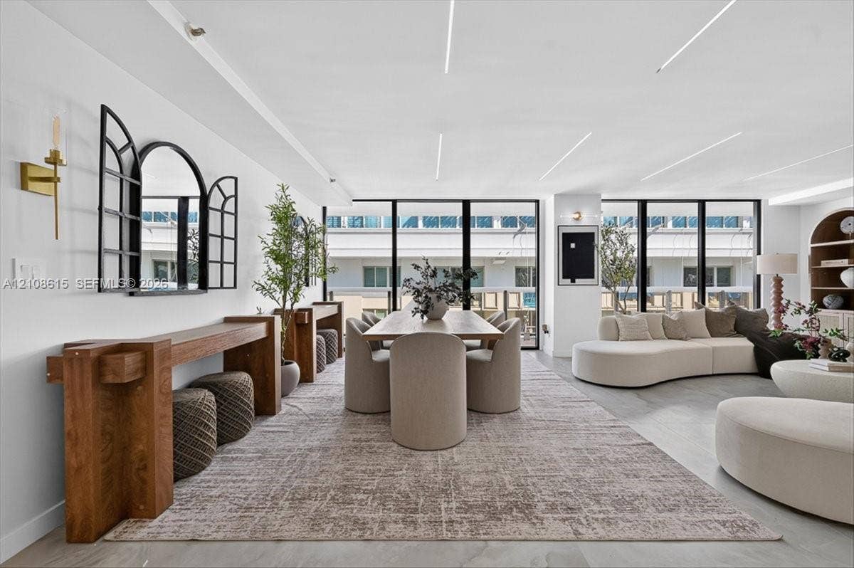 9455 Collins Avenue, #1201, Surfside, FL 33154 Open-concept space featuring floor-to-ceiling black-framed windows, integrated recessed linear ceiling lighting, light-toned stone-finish flooring, and a built-in arched wooden shelving unit